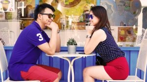 A couple at a coffee table smiling after learning about the benefits of moving in together with your partner